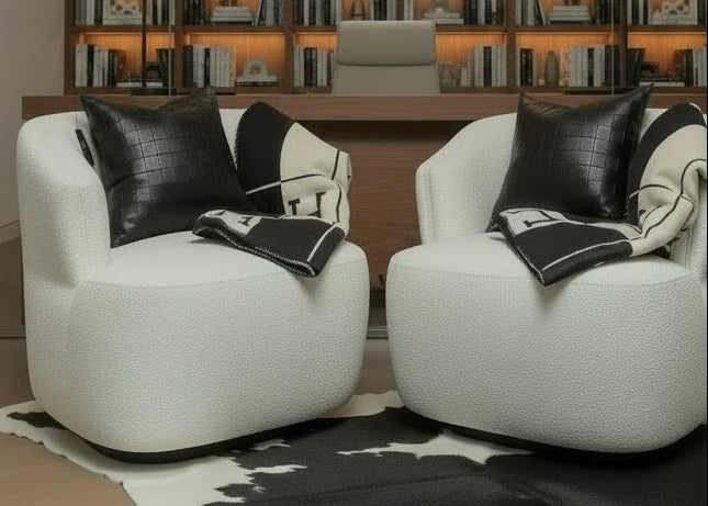 A cream bouclé armchair styled with eikhomeco.com black leather accent pillow, cream knit throw pillows and a matching black-and-cream throw blanket featuring a large white 'H' on a black and white cowhide rug.